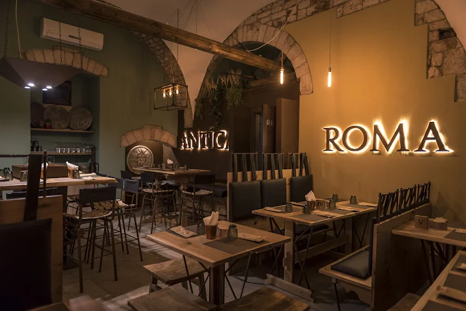 Sala interna di Antica Roma Pub Pizzeria con tavoli in legno e insegna illuminata